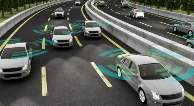 A computer-generated image depicting a multi-lane highway with several silver cars. Blue and green waves radiate from the vehicles, illustrating the concept of self-driving cars using sensors and vehicle-to-vehicle communication.